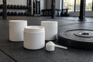 Tre bokser kreatin monohydrat med en måleskje hvitt pulver ved siden av en vektskive